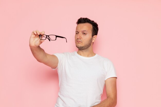 Une vue de face jeune homme en t-shirt blanc tenant des lunettes de soleil optiques