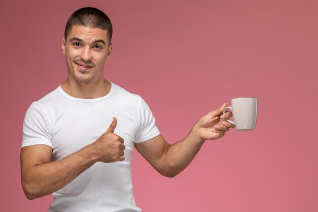 Vue de face jeune homme en t-shirt blanc tenant une tasse de café sur le fond rose