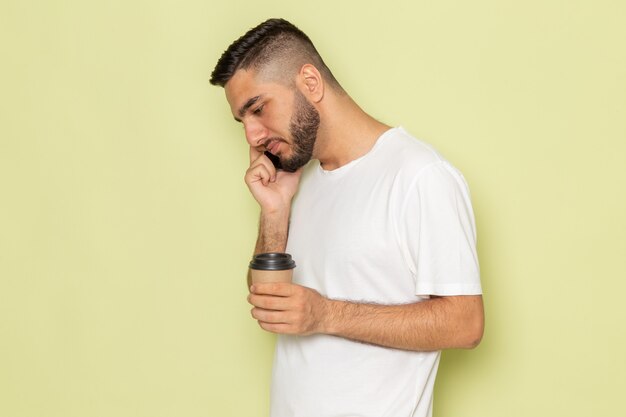 Une vue de face jeune homme en t-shirt blanc tenant une tasse de café et parler au téléphone