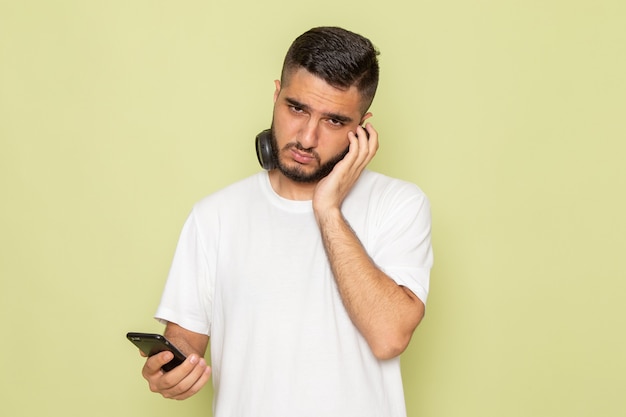 Une vue de face jeune homme en t-shirt blanc tenant le téléphone et écouter de la musique