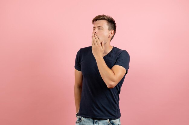 Vue de face jeune homme en t-shirt foncé et jeans bâillant sur fond rose