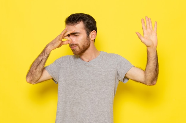 Une vue de face jeune homme en t-shirt gris couvrant son nez sur le mur jaune modèle de couleur expression émotion homme