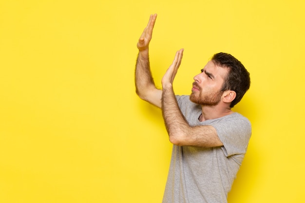 Une vue de face jeune homme en t-shirt gris avec expression de peur sur le modèle de couleur de l'émotion expression homme mur jaune