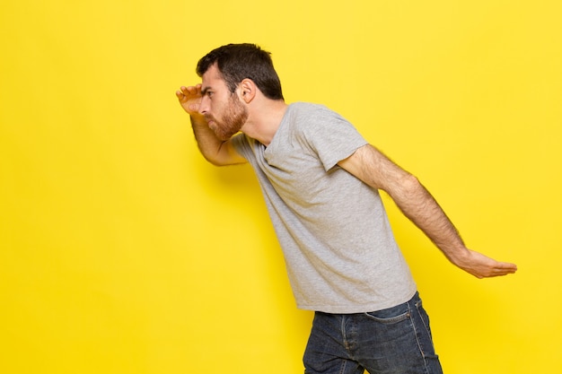 Une vue de face jeune homme en t-shirt gris avec une expression de recherche sur le modèle de couleur expression émotion homme mur jaune