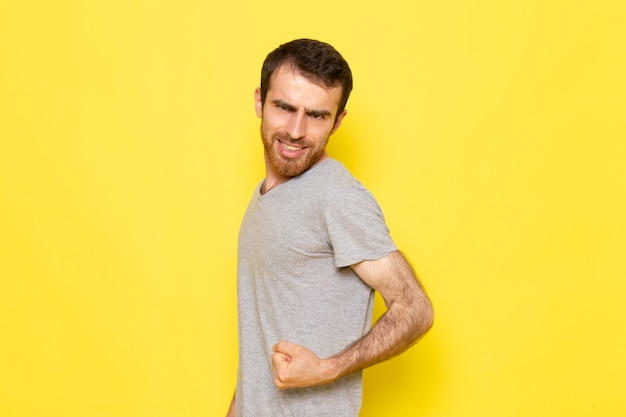 Une vue de face jeune homme en t-shirt gris fléchissant sur le mur jaune expression de l'homme modèle couleur émotion