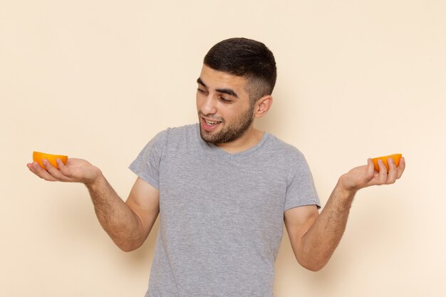 Vue de face jeune homme en t-shirt gris et jean bleu souriant et tenant des rondes orange sur beige