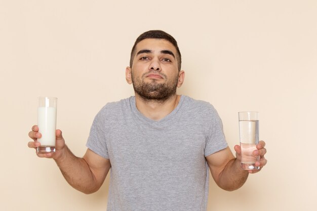 Vue de face jeune homme en t-shirt gris et jean bleu tenant de l'eau et du lait sur beige