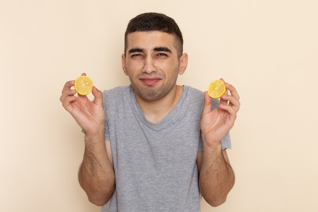 Vue de face jeune homme en t-shirt gris de manger des anneaux de citron aigre sur beige
