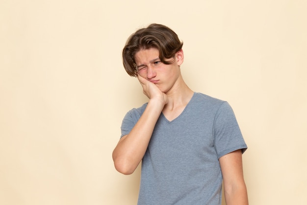 Une vue de face jeune homme en t-shirt gris posant ayant mal aux dents