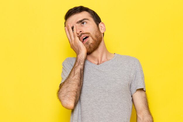 Une vue de face jeune homme en t-shirt gris posant avec une expression fatiguée sur le modèle de couleur homme mur jaune