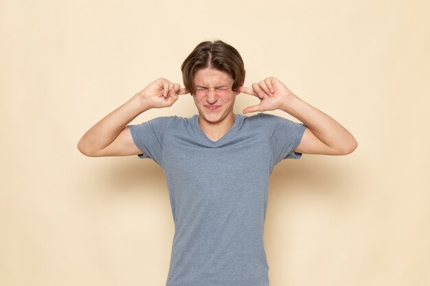 Une vue de face jeune homme en t-shirt gris posant en fermant les oreilles
