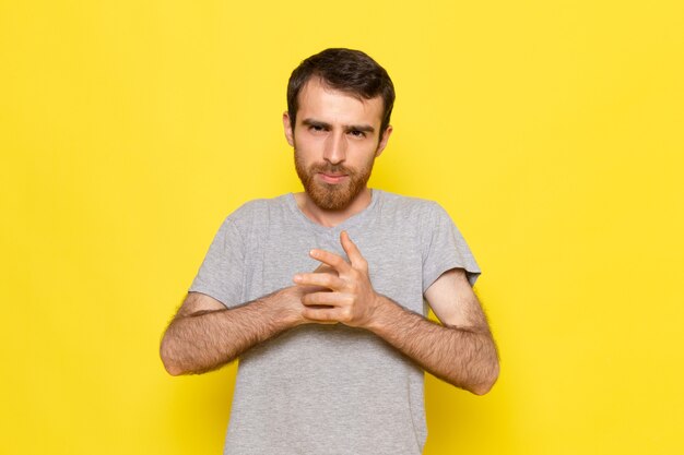 Une vue de face jeune homme en t-shirt gris posant sur le modèle de couleur expression émotion homme mur jaune