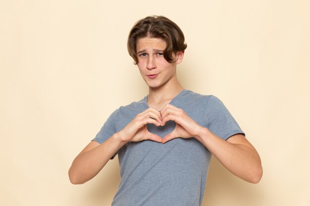 Une vue de face jeune homme en t-shirt gris posant montrant signe de coeur