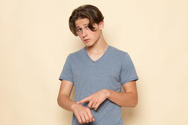 Une vue de face jeune homme en t-shirt gris posant en soulignant dans son poignet