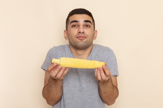 Vue de face jeune homme en t-shirt gris tenant du maïs cru sur beige