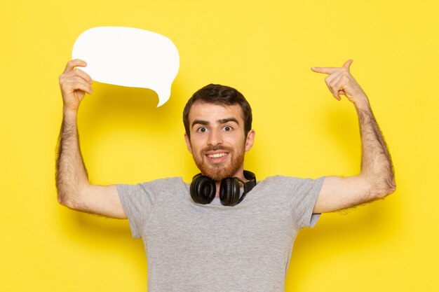 Une vue de face jeune homme en t-shirt gris tenant une pancarte blanche sur le modèle de couleur expression émotion homme mur jaune