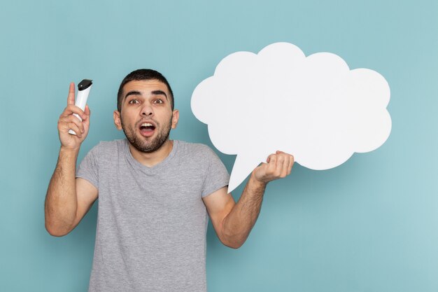 Vue de face jeune homme en t-shirt gris tenant une pancarte blanche et un rasoir électrique sur la glace bleu