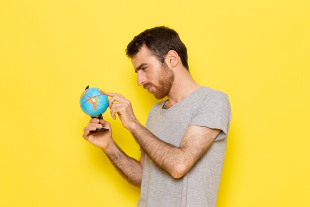 Une vue de face jeune homme en t-shirt gris tenant petit globe sur le mur jaune homme couleur modèle émotion vêtements