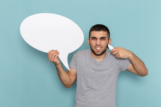 Vue de face jeune homme en t-shirt gris tenant un rasoir électrique avec grand panneau blanc sur homme bleu glace