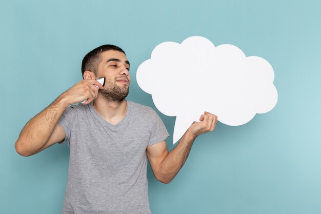 Vue de face jeune homme en t-shirt gris tenant un rasoir électrique avec un panneau blanc sur l'homme bleu glace