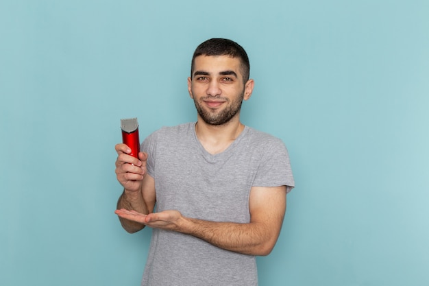 Vue de face jeune homme en t-shirt gris tenant un rasoir électrique sur le rasoir à cheveux en mousse barbe bleu glace