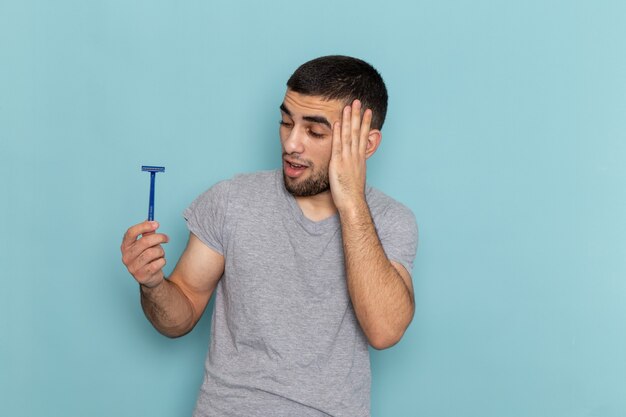 Vue de face jeune homme en t-shirt gris tenant le rasoir et posant sur la barbe de rasage bleue