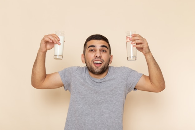 Vue de face jeune homme en t-shirt gris tenant un verre de lait d'eau sur beige