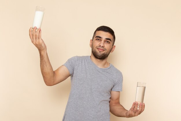 Vue de face jeune homme en t-shirt gris tenant un verre de lait d'eau sur beige
