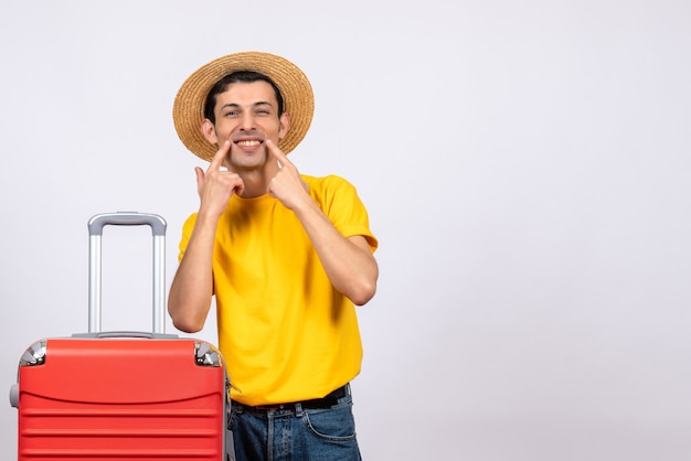 Vue de face jeune homme avec t-shirt jaune et chapeau de paille pointant sourire