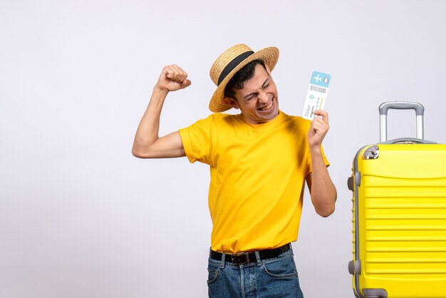 Vue de face jeune homme en t-shirt jaune debout près de valise jaune tenant un billet exprimant son bonheur