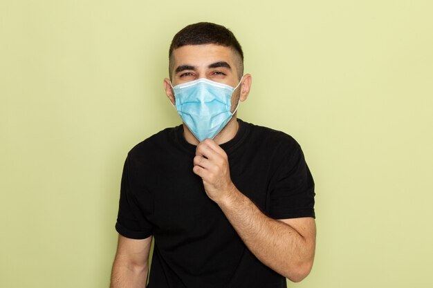 Vue de face jeune homme en t-shirt noir portant un masque stérile sur vert