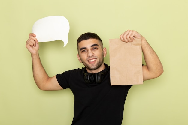 Vue de face jeune homme en t-shirt noir tenant une pancarte blanche et un emballage alimentaire sur vert