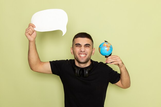 Vue de face jeune homme en t-shirt noir tenant une pancarte blanche et petit globe avec un large sourire sur vert