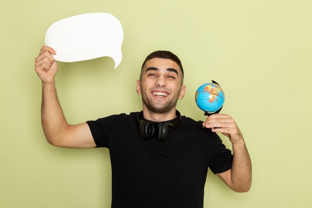 Photo gratuite vue de face jeune homme en t-shirt noir tenant une pancarte blanche et petit globe avec sourire sur vert