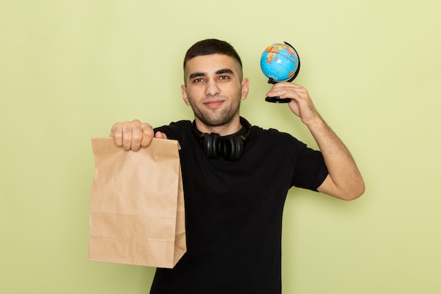 Vue de face jeune homme en t-shirt noir tenant le paquet alimentaire et petit globe sur vert