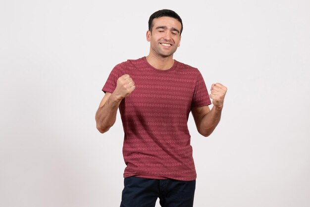 Vue de face jeune homme en t-shirt posant et se réjouissant sur fond blanc