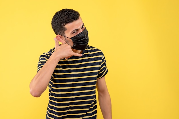 Vue de face jeune homme avec t-shirt rayé noir et blanc faisant appelez-moi signe de téléphone fond jaune place libre