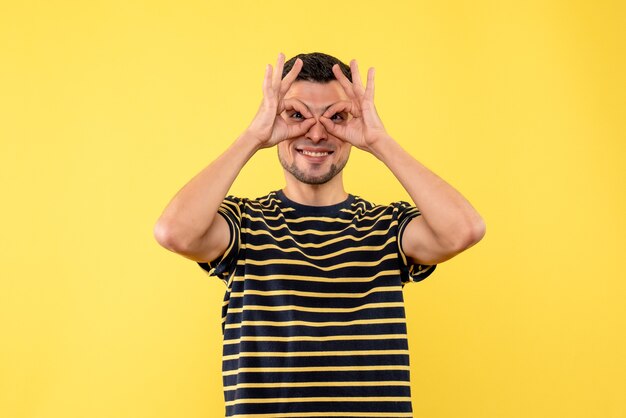 Vue de face jeune homme en t-shirt rayé noir et blanc faisant des mains jumelles sur fond isolé jaune