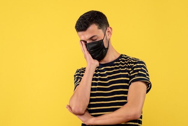 Vue de face jeune homme en t-shirt rayé noir et blanc mettant la main sur son visage fond jaune