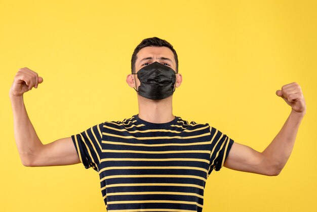 Vue de face jeune homme avec t-shirt rayé noir et blanc montrant les muscles du bras fond jaune