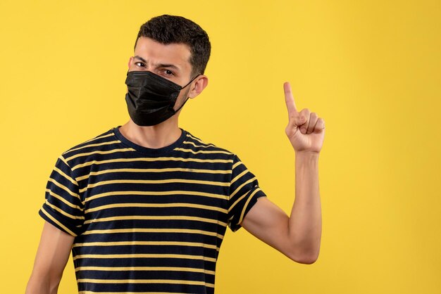 Vue de face jeune homme en t-shirt rayé noir et blanc pointant avec le doigt sur fond jaune