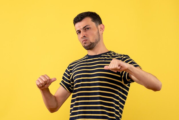 Vue de face jeune homme en t-shirt rayé noir et blanc pointant sur lui-même fond isolé jaune