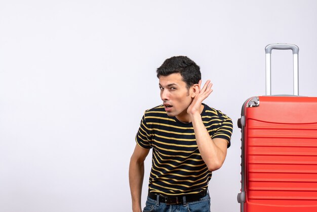 Vue de face jeune homme avec t-shirt rayé et valise en écoutant quelque chose