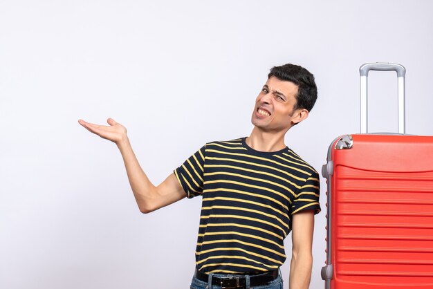 Vue de face jeune homme avec t-shirt rayé et valise rouge montrant quelque chose