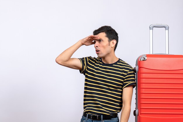 Vue de face jeune homme avec t-shirt rayé et valise rouge observation