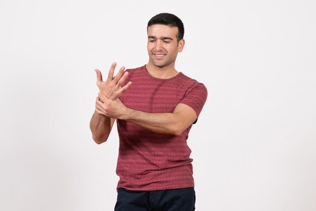 Vue de face jeune homme en t-shirt rouge foncé debout sur un bureau blanc