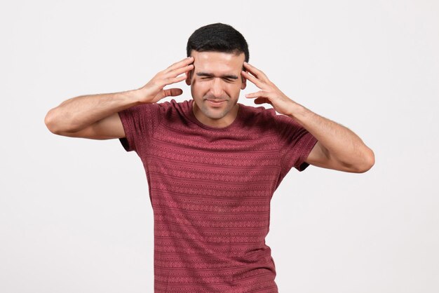 Vue de face jeune homme en t-shirt rouge foncé debout sur un bureau blanc