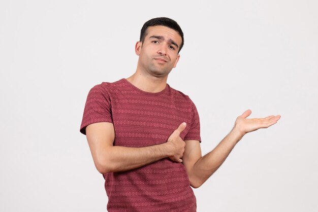 Vue de face jeune homme en t-shirt rouge foncé debout sur un bureau blanc