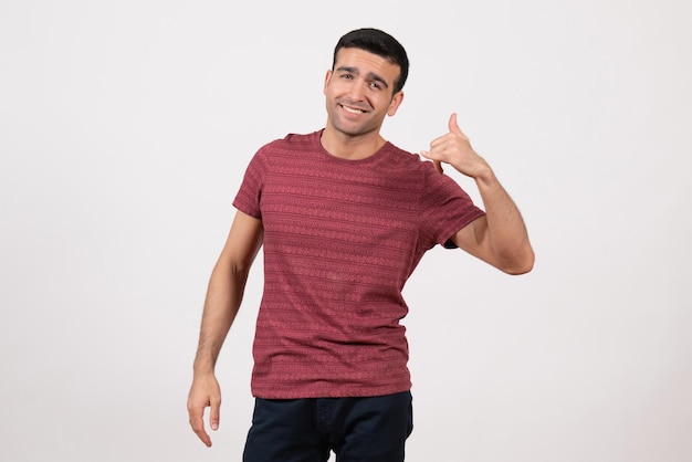 Vue de face jeune homme en t-shirt rouge foncé souriant et debout sur fond blanc