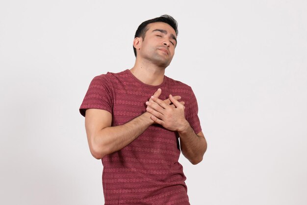 Vue de face jeune homme en t-shirt rouge foncé touchant son cœur sur fond blanc